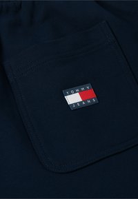 Poche en tissu bleu marine foncé avec un écusson Tommy Jeans présentant des rayures rouges, blanches et bleu marine cousues au centre de la poche.