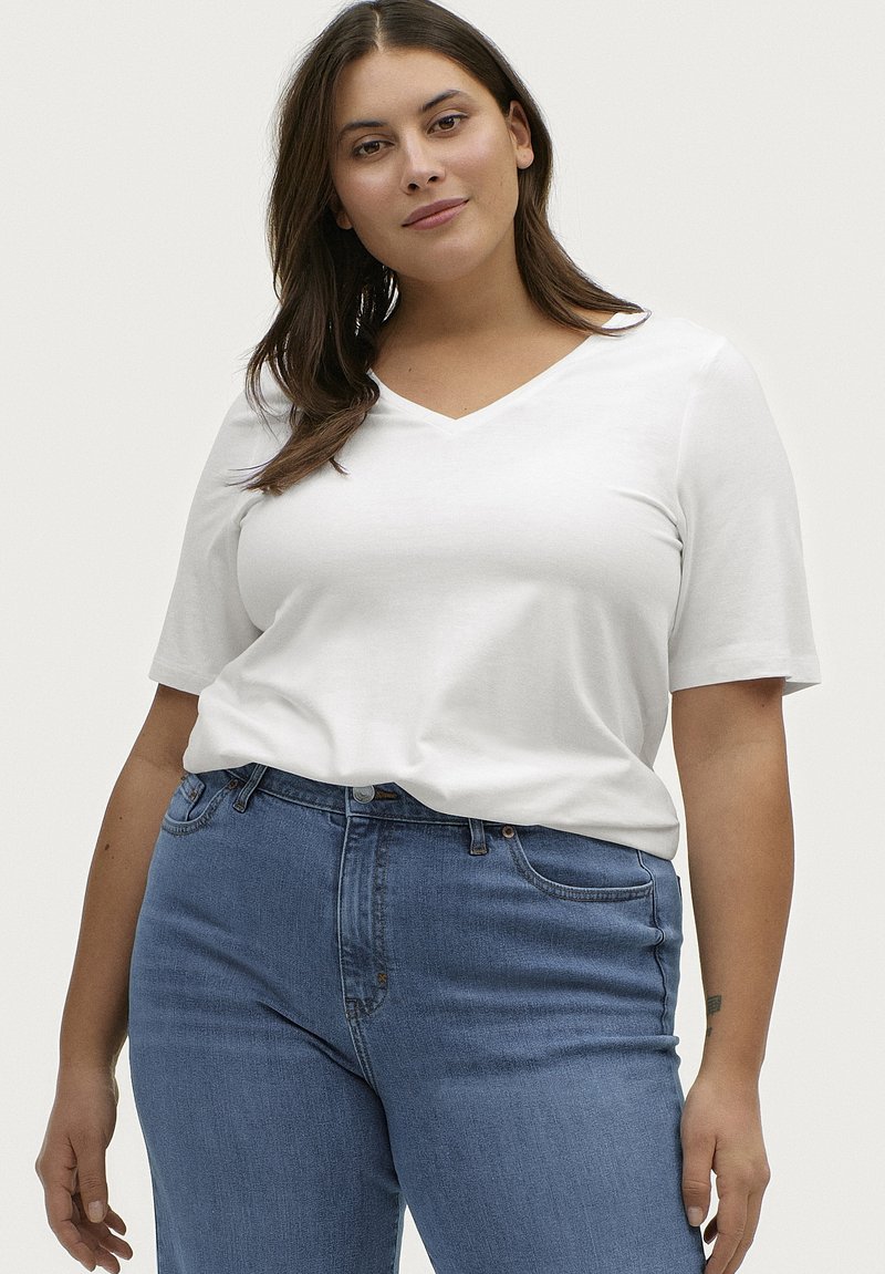 Hvid V-hals T-shirt lavet af blødt stof, kortærmet og afslappet pasform, parret med højtaljede blå denim jeans.