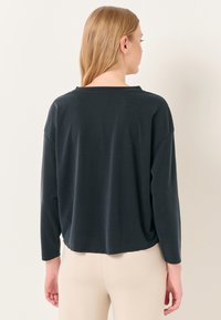 Top nero a maniche lunghe con vestibilità rilassata, spalle scese e orlo arrotondato. Tessuto morbido con cuciture minime e una sottile texture.