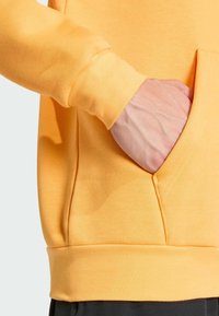 Pomarańczowy sweatshirt z kieszenią kangurzą i ściągaczami. Gładka tekstura i wygodny krój, podkreślone starannym przeszyciem.