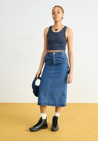 Ein enges, dunkelblaues geripptes Tanktop kombiniert mit einem hoch taillierten, knielangen Jeansrock. Schwarze High-Top Sneakers und eine strukturierte dunkle Tasche runden den Look ab.