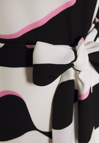 Tissu noir, blanc et rose à motif noué en un nœud ou un détail de bow sur un vêtement.