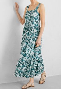 Květinové maxi šaty v tyrkysové a bílé barvě, se čtvercovým výstřihem, širokými ramínky, vrstevnatou sukní a lehkým materiálem. Doplněné béžovými sandály.