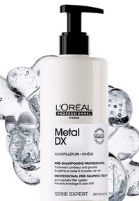 L'Oréal Metal DX pre-shampoo i en hög, ogenomskinlig vit flaska med en svart pump. Innehåller produktinformation i svart text, omgiven av bubblor.