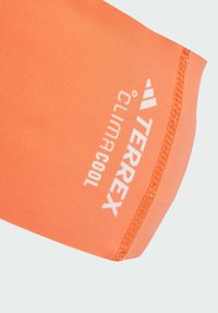 Oranžové atletické tričko s hladkou texturou, s bílým logem "TERREX" a "ClimaCool" poblíž švu.