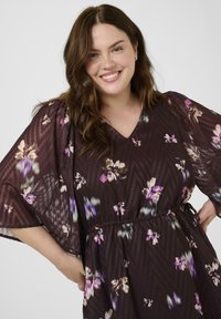 Sötétbarna, virágmintás, mély dekoltázsú, rövid ujjú ruha lila, krémszínű és zöld színekkel. Könnyű, laza anyag, derékban behúzott.