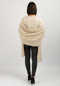Beige strikket cardigan draperet over skuldrene, med åben front og lang ryg. Sættes sammen med sorte skinny jeans og sorte højhælede sko.