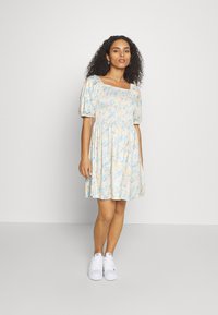Vestido floral em cores pasteis com decote quadrado, mangas curtas bufantes e cintura franzida, combinado com ténis brancos.