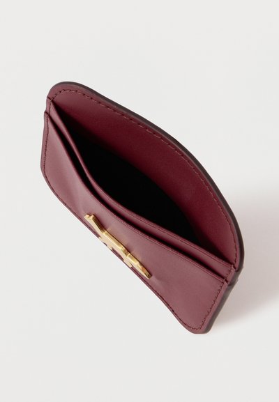 Καρτοφύλακας από μπορντό δέρμα με λεία υφή, διαθέτει κλείσιμο με μεταλλικό κλιπ σε χρυσό τόνο, εσωτερική θήκη και ραμμένες άκρες.