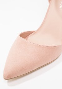 Gros plan sur une chaussure plate pour femme en suède rose à bout pointu, avec une texture lisse et des coutures nettes le long du bord.