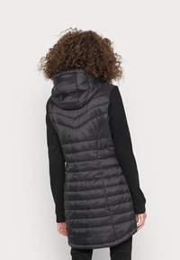 Gilet imbottito nero con cappuccio, caratterizzato da un design trapuntato con cuciture verticali e diagonali, che arriva fino a metà coscia.