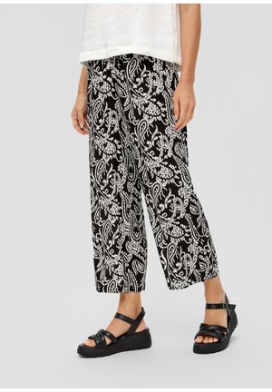 Persoon draagt zwart-witte, wijde broek met bloemenpatroon en zwarte platformsandalen met enkelbandjes.