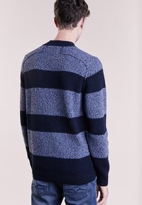 Marinblå och ljusblå randig tröja i en strukturerad stickning, med rundad halsringning och ribbade ärmavslut. Visad bakifrån.