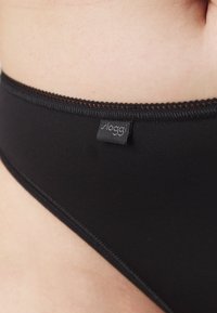 Zwarte bikini bottom met een gladde textuur, voorzien van een delicaat contrasterend gestikt randje en een klein merketiket dat op de tailleband is geplaatst.