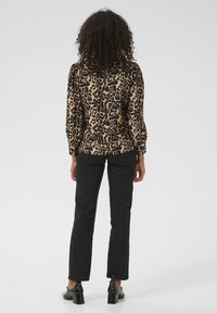 Leopard print blouse made of smooth fabric, with a black and beige pattern. Paired with fitted black pants and glossy black heels.