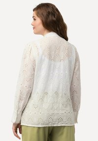 Witte geborduurde blouse met bloem- en geometrische uitsnijdingen, lange mouwen en een klassieke kraag, gemaakt van een lichtgewicht, textuurstof.