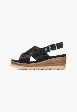 Sandalias de cuña de cuero negro con diseño floral recortado, hebilla ajustable y suela plataforma de madera clara con textura.
