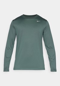 Dlouhý rukáv sportovní tričko v tmavě zelené tkanině se hladkým povrchem. Vybaveno zaobleným výstřihem a malým bílým logem Nike na hrudi.