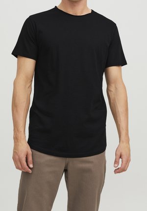 Czarna bawełniana koszulka z krótkim rękawem, okrągłym dekoltem, lekko postrzępionymi brzegami i luźnym krojem, połączona z jasnobeżowymi spodniami.