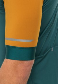 Korte mouwen sporttop met een geel-oranje bovenmouw en een teal onderste mouw, voorzien van een reflecterende zilveren streep bij de manchetten.