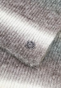 Maglione lavorato a maglia con un gradiente dal grigio chiaro al bianco. Presenta un motivo a coste testurizzato e un accento circolare con un logo in argento.