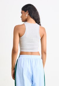 Hallide hallusmidiga hall värviga lühike topp, millel on sooniline tekstuur ja laiad õlapaelad, koos helesiniste laialdaste pükstega, millel on rohelised külgelintide triibud.