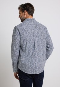 Camicia a scacchi blu e bianca con maniche lunghe, colletto a bottoni, tessuto testurizzato e una vestibilità comoda, indossata con jeans scuri.