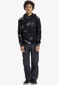 Svart hoodie med olika färgglada mönster, inklusive ett spindelnät, tärningar och olika grafik. Matchad med mörk denimjeans och svarta skor.