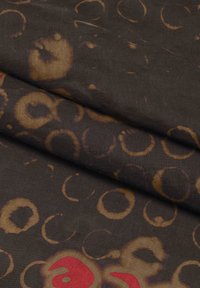 Tessuto con uno sfondo marrone scuro e motivi circolari in marrone chiaro e rosso. Il tessuto ha una consistenza liscia e una leggera lucentezza.