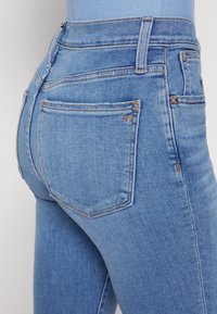 Jeans de cintura alta azul claro com um corte ajustado. Feitos de denim, apresentam bolsos traseiros com costura em contraste e uma textura suave.