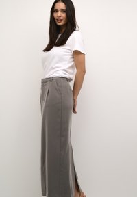 Light gray wide-leg trousers with front pleats, side slits, and a tailored fit, paired with a plain white t-shirt. Smooth fabric texture.