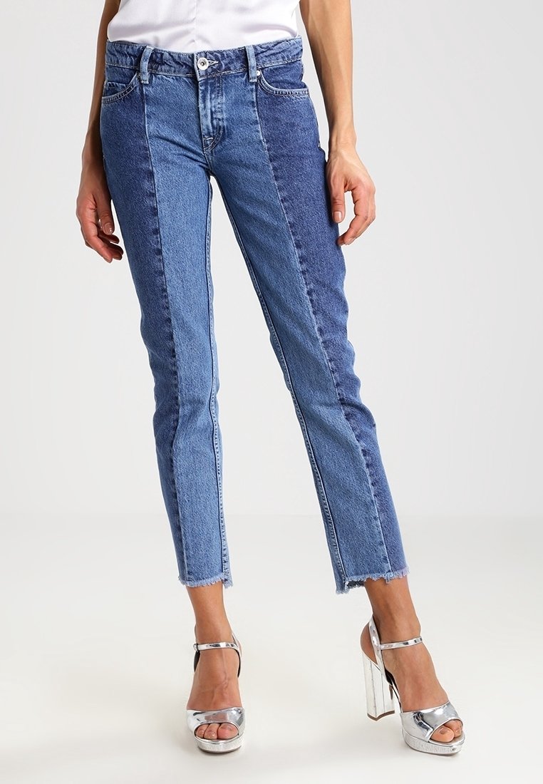 Siniset farkut, joissa on väriblokki-kuvio vaaleansinisin ja tummansinisin paneelein, kapea malli, lyhyt pituus ja rispaantuneet reunat.