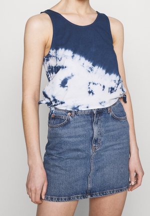 Liu navy ja valge sidumisega top, millel on ümmargune kaelus, koos helesinise denimmikro seeliku ja küljetaskutega, millel on nööbiga kinnitamine.