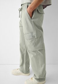 Hellgraue Cargo-Hosen mit elastischem Bund und Kordelzug. Verfügen über seitliche Taschen und Knopf-Cargotaschen an den Oberschenkeln.