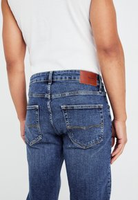 Džíny z denimu s tmavomodrým prádlom, so koženou nášivkou na zadnej strane, dvoma zadnými vreckami a vyšívanými detailmi.