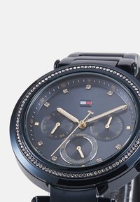Reloj analógico negro con caja redonda y bisel de cristal. Presenta una esfera oscura con acentos dorados, marcadores de fecha y dos subesferas.