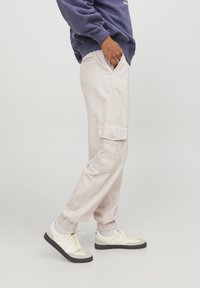 Světlé cargo kalhoty s elastickými manžetami, obsahující boční kapsy a plochý přední design, doplněné bílými a černými teniskami.