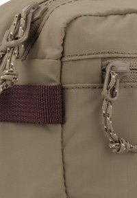 Borsa in nylon color beige caratterizzata da una superficie texturizzata, chiusura con zip e una tracolla in tessuto maroon con dettagli in paracord marrone e crema.