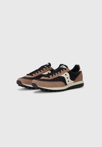 Brune og sorte semskede sneakers med sorte snørebånd, et hvidt logo og stribede gummisåler med buede detaljer og perforeringer.