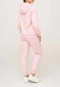 Sweat à capuche rose clair et joggeurs assortis en tissu doux, avec une poche avant et des poignets côtelés, offrant une coupe décontractée.