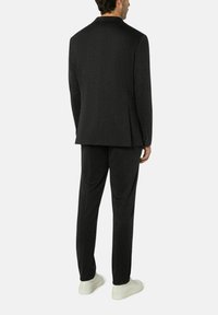Ein anthrazitgrauer Blazer und passende Hose aus strukturiertem Stoff. Der Blazer hat einen Reverskragen und Knopfmanschetten. Kombiniert mit weißen Sneakers.