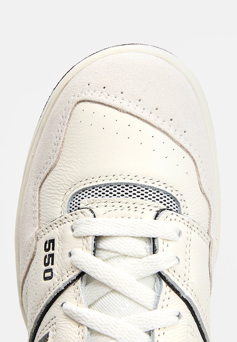 Weißer Sneaker mit einem Obermaterial aus glattem Leder und Wildleder, das über Perforationen, eine Mesh-Zunge und einen schwarzen Akzent mit der Aufschrift "550" an der Seite verfügt.