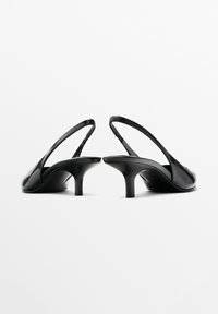 Svarta slingback-klackar i glänsande läder, med en smal klack och öppen baksida. Slät yta med minimalt med hårdvara.