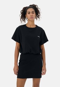 Czarny bawełniany t-shirt z krótkim rękawem i okrągłym dekoltem, zestawiony z czarną spódnicą. Charakteryzuje się subtelnym logo na koszulce.