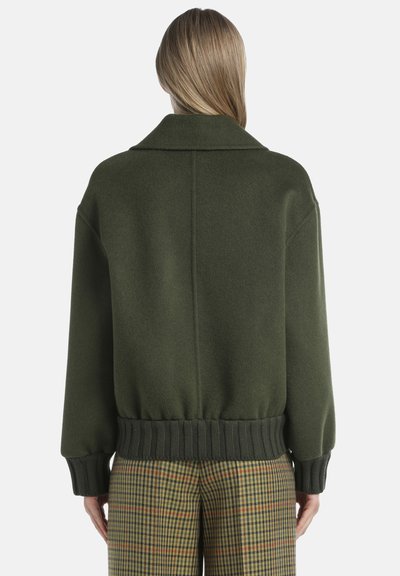 Zöld gyapjúkeverék oversized zákó, gallérral, bordázott mandzsettával és aljjal. Simasága és laza szabása jellemzi. Kockás nadrággal párosítva.