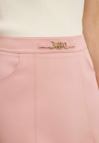 Roze hoge taille broek is gemaakt van een gladde stof, heeft een subtiele glans, voorzakken en een decoratieve goudkleurige gesp als detail.