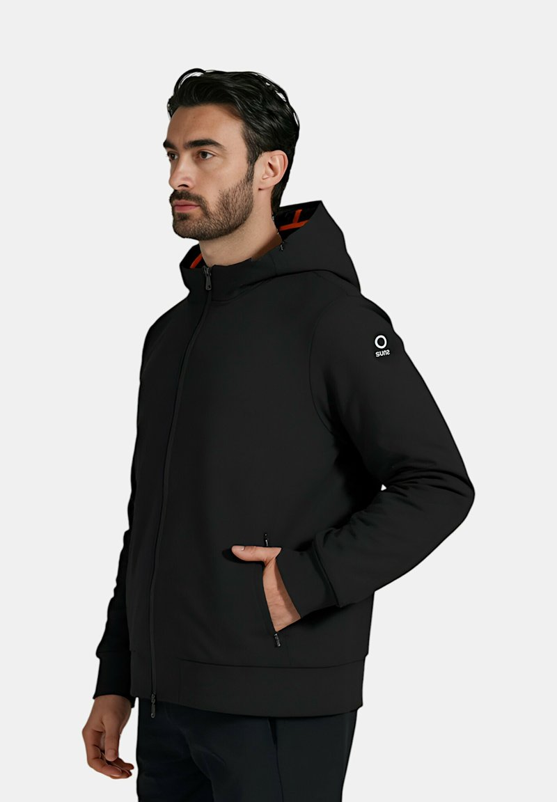 Felpa nera con zip e vestibilità strutturata, dotata di un rivestimento arancione a contrasto, due tasche laterali e un logo accentato sulla manica.