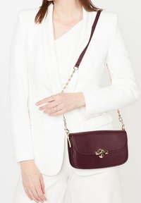 Borsa a tracolla bordeaux con patta arrotondata, accessori in oro e tracolla a catena, realizzata in materiale sintetico liscio.