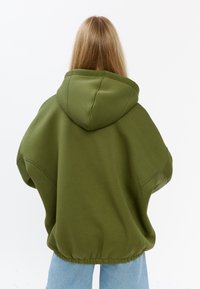 Übergroßer grüner Hoodie mit Kapuze, ausgestattet mit einem gerippten Saum, überschnittenen Schultern und einer weichen Textur. Rückansicht mit nahtlosem Design.