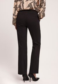Czarne dopasowane spodnie o prostym kroju, wykonane z gładkiego materiału. Posiadają smukłą sylwetkę i są zestawione z czarnymi szpilkami.